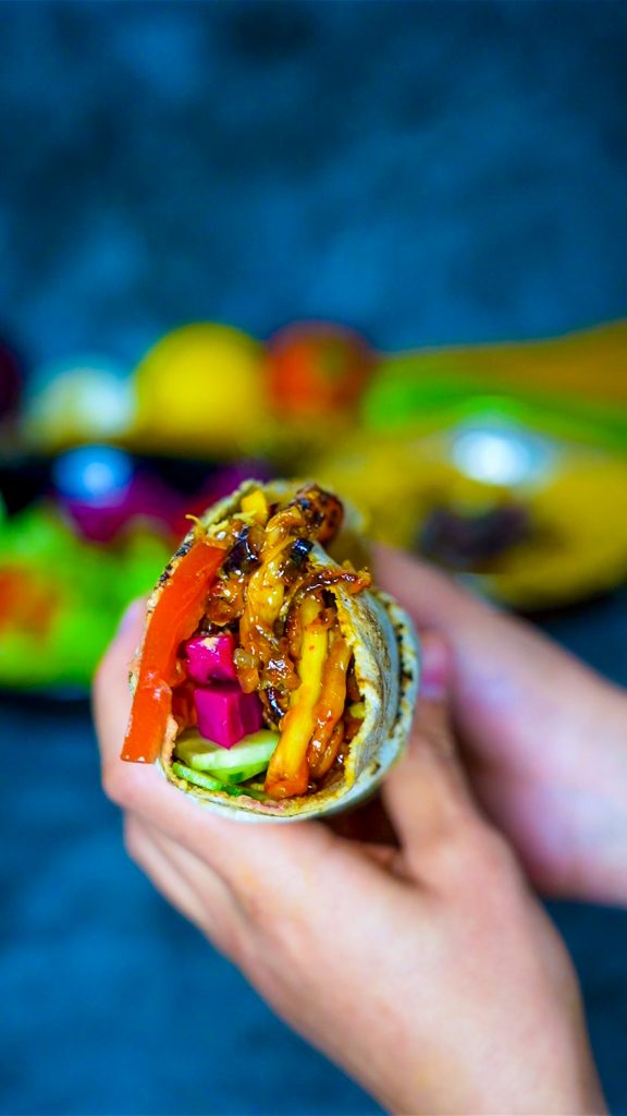 Veganes Shawarma mit Austernpilzen, serviert mit cremigem Hummus und frischen Kräutern.