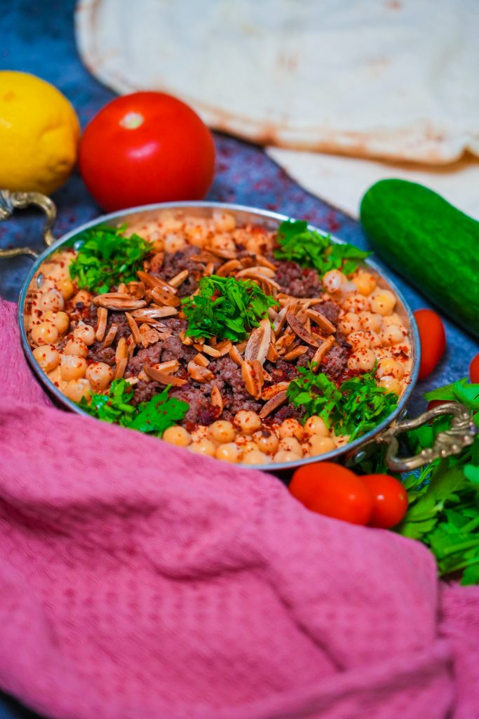 Hummus mit Hackfleisch, gerösteten Mandeln und frischer Petersilie, angerichtet auf einem Teller.