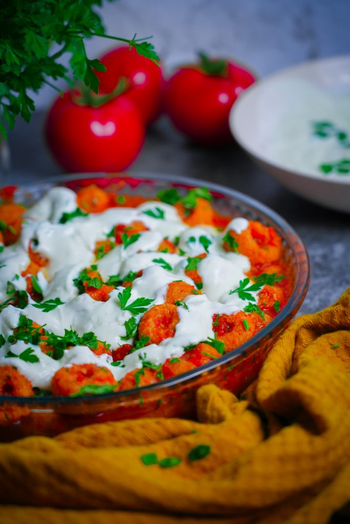 Fellah Köftesi – Türkische Bulgurbällchen serviert in würziger Tomatensoße, garniert mit frischer Petersilie und Joghurtsoße.