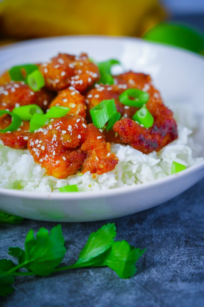 Knusprige Garnelen mit würziger Soße und Reis, garniert mit Frühlingszwiebeln und Sesam.