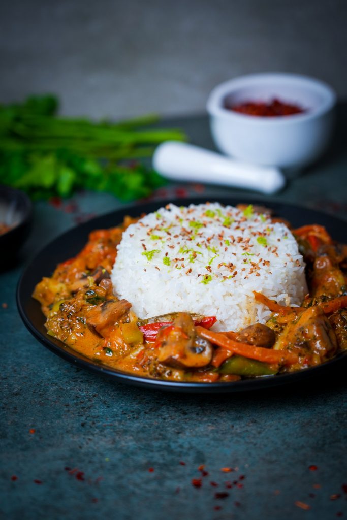 Bunte Gemüse-Curry-Pfanne mit Kokosmilch und Limettenabrieb, serviert mit Reis und geröstetem Sesam.