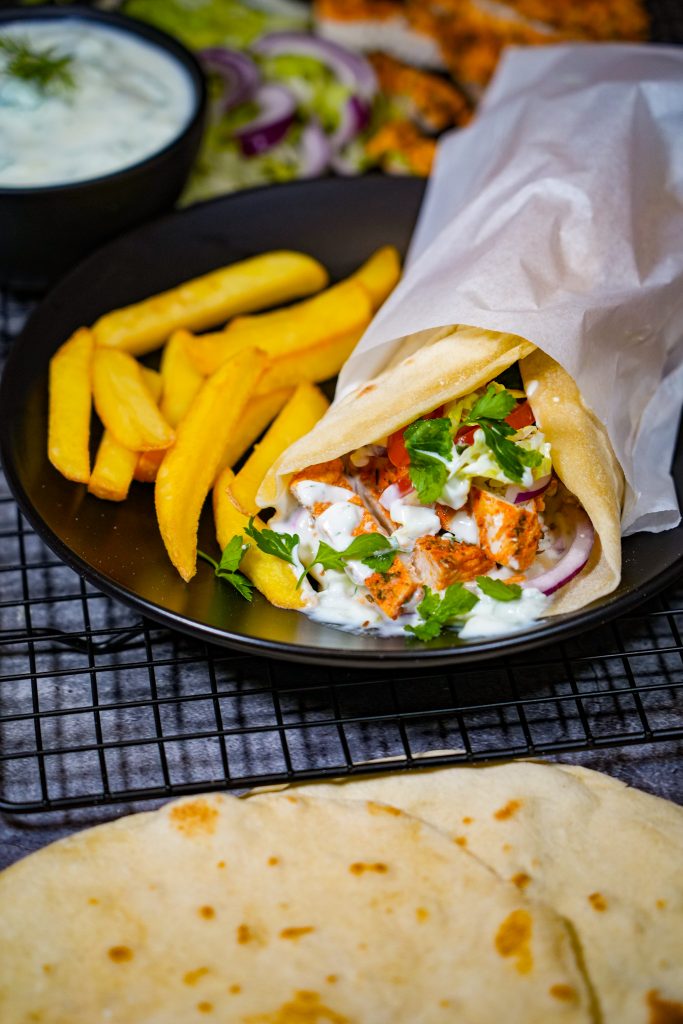 Gyros-Wraps mit saftigem Hähnchen, Tzaziki und frischem Gemüse, serviert mit Pommes.