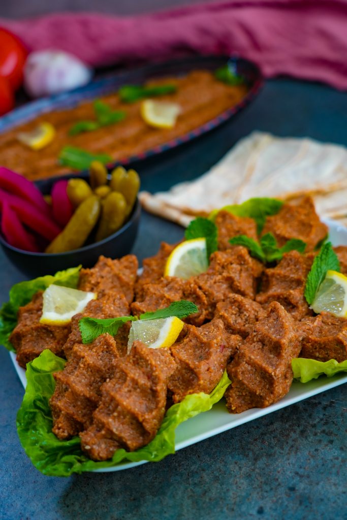 Ein Teller mit rohem Kibbe Nayyeh, dekorativ angerichtet mit Olivenöl, Minzblättern und einer glatten Oberfläche mit Gabelmuster.