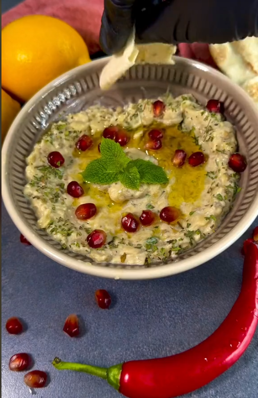 Cremiger Mutabbal-Dip, angerichtet mit Olivenöl und Granatapfelkernen, serviert in einer Schale.
