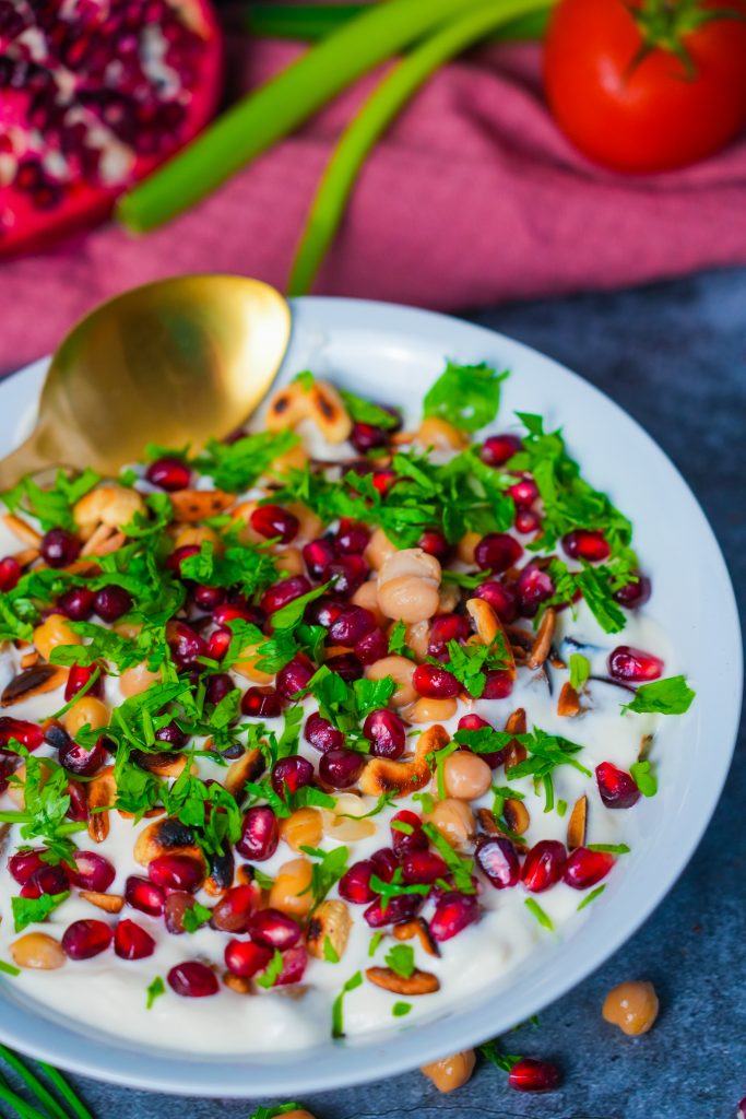 Ein stilvoll angerichtetes Fatteh mit knusprigem Brot, Kichererbsen, Joghurtsoße, gerösteten Nüssen und frischen Granatapfelkernen.