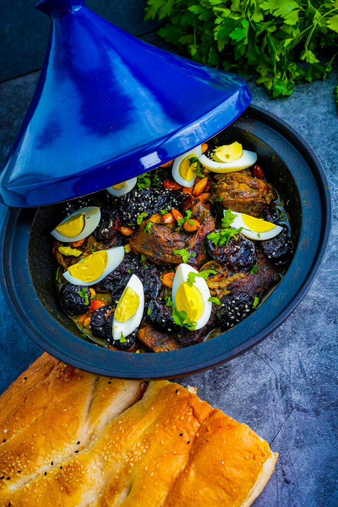 Traditionelle Tajine mit Lamm, Pflaumen, Mandeln und Fladenbrot, angerichtet auf einem kunstvollen marokkanischen Teller.