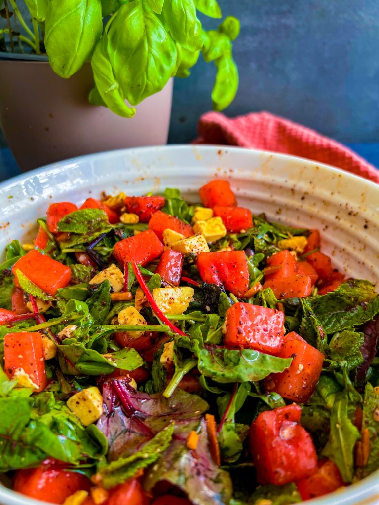 Ein sommerlicher Salat mit Melonenwürfeln, Feta, Minze und gerösteten Mandelstiften, serviert auf einem Bett aus Salatmix.