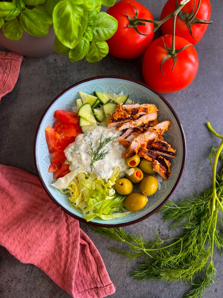 Eine bunte Gyrosbowl mit saftigem Hähnchen, Tzaziki, frischem Gemüse und fluffigem Reis, dekoriert mit Oliven und Feta.